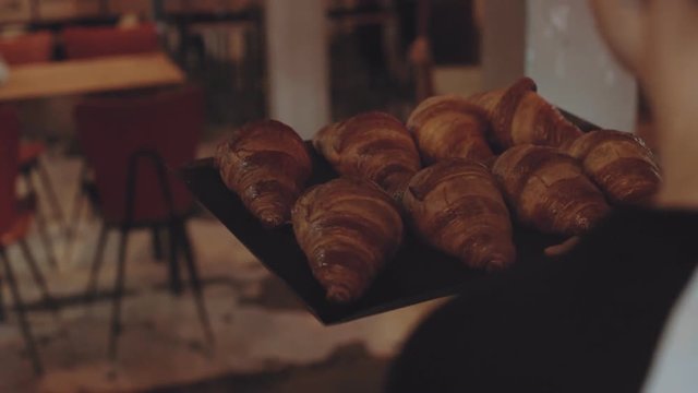 Camera follows waiter or baker carry tray full of fresh just baked crispy french croissants with butter through cafe or restaurant to table. Hospitality small business idea, local company