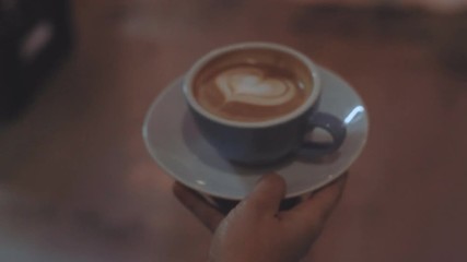 Camera follows waiter who carries fresh and perfectly made coffee with latte art on top, made out of fresh and organic fairtrade beans, through cafe or bar to satisfied customer at big table