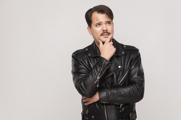 Hmm, lets my think. Pleased, confusion concept. Man in black jacket looking away, touching chin and thinking.