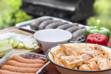 Kiełbasa, kaszanka oraz surowe mięso kurczaka w przyprawach stoi w miskach na stole. © Tomasz