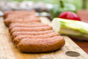 4.	Kiełbasa leży na drewnianej desce obsypana przyprawami do grilla. Surowe warzywa w tle.