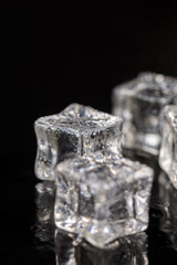 Ice cubes with drops of water on the black background with reflections