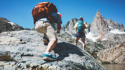 Young backpackers couple rock climbing together in stunning mountain wilderness near the snowy lake