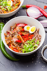 Noodles with chicken's meat, chili peppers and eggs in bowl on dark stone background. Asian Cuisine Pasta. Top view. 