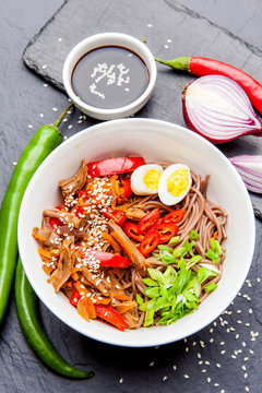 Noodles with chicken's meat, chili peppers and eggs in bowl on dark stone background. Asian Cuisine Pasta. Top view. 