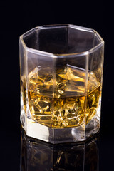 Octagon square glass with whiskey and ice cubes on the black background with reflections