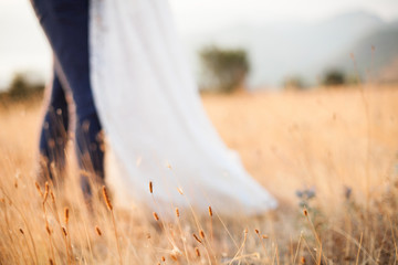 The bride and the groom are hugging and standing on field at blurred background of mountains and...