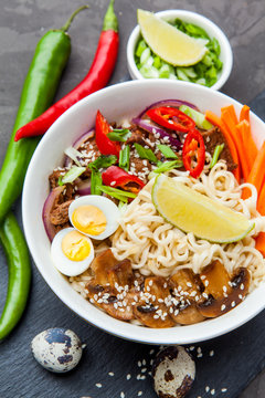 Noodles with beef meat, chili peppers and mushrooms in bowl on dark stone background.  