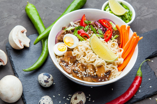 Noodles with beef meat, chili peppers and mushrooms in bowl on dark stone background.  