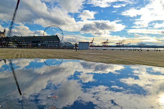 Landscape view of the waterfront in Seattle, Washington, USA from a wooden pier after rain with a wide pudle in which the clouds are reflected.  