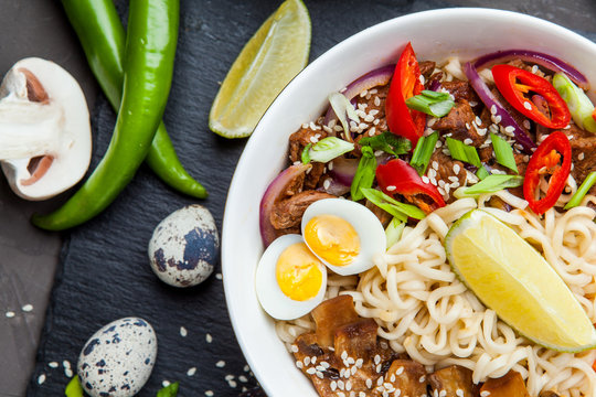 Noodles with beef meat, chili peppers and mushrooms in bowl on dark stone background. 