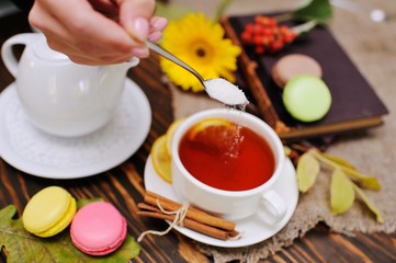 hand with a teaspoon pours sugar into the tea with a lemon close-up against a backdrop of macaroons...