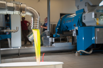Finished olive oil running from a steel tap into a funnel inside an oil mill