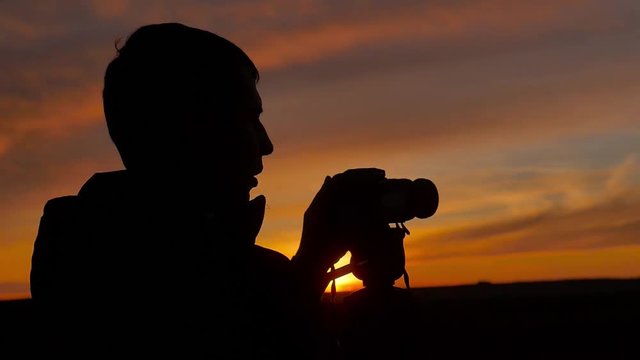 Photographer silhouette close-up, young cameraman shoots photos and videos, dusk.