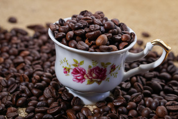 Coffee cup with purple flowers filled with beans surounded with beans on sackclothe