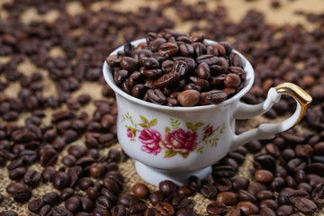 Coffee cup with purple flowers filled with beans surounded with beans on sackclothe