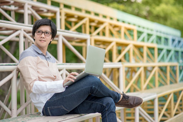 Young Asian student man sitting on grandstand and using laptop computer, university lifestyle in college, educational concepts