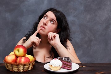 Young attractive overweight woman choosing  between healthy foods and sweets, copy space. Dieting,...