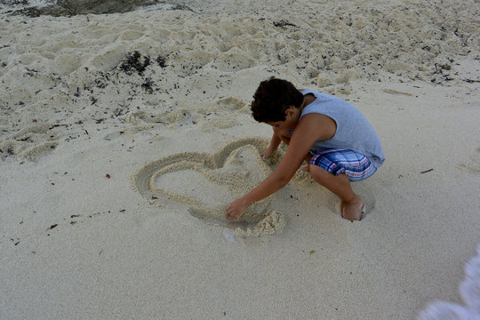 El chico dibuja  corazon de arena en la playa.