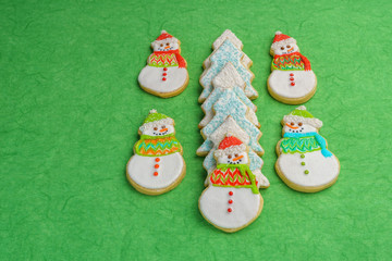 Christmas snowman and tree cookies on green background.