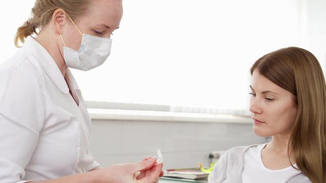 Dentist talking with woman patient in clinic. Female professional doctor at work. Showing cape for teeth explaining medical procedures. Dental equipment on background. Dental check up