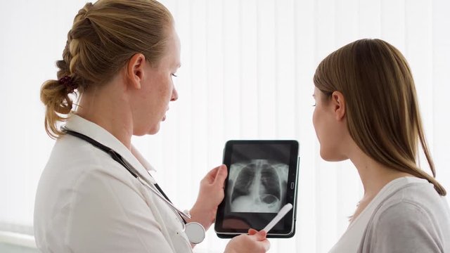 Woman physician with stethoscope talking with female patient in clinic. Female professional doctor at work. Showing X-ray on tablet. Health care