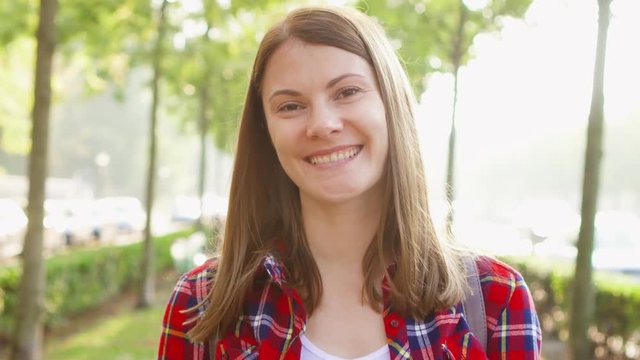 Portrait of happy cheerful young woman enjoying nature. Walking in green autumn park smiling at camera