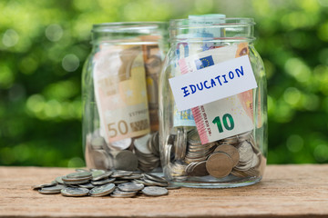 glass jar bottles with full of coins labeled as Education as education or savings for school concept