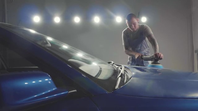 Master polishes the deep blue sport car via polish mashine in a car workshop