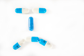 White and blue pills or capsules on white background forming a sad, frown, angry face