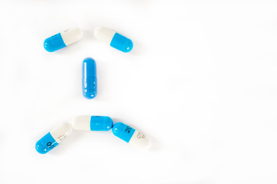 White and blue pills or capsules on white background forming a sad, depressed, frowny face