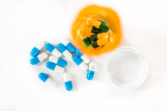 Overhead View Of White And Blue Pills Or Capsules Scattered And In Orange Prescription Bottle