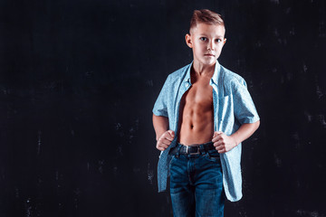 Boy in shorts posing for camera and showing his abs while standing on dark wall background.
