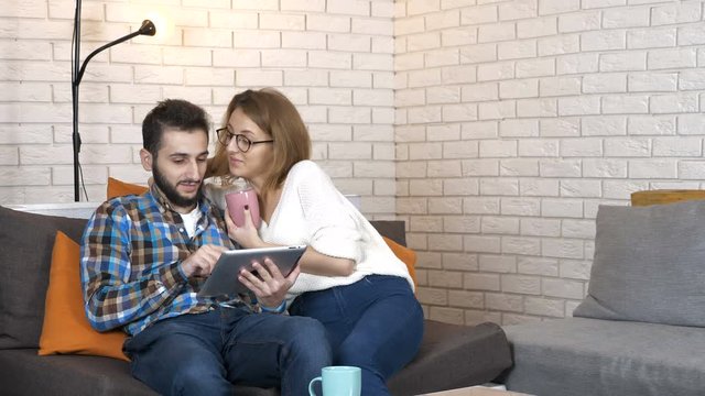 Happy young couple sitting on the couch with a tablet and discuss 50 fps
