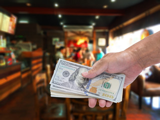 Fototapeta premium Man hand holding dollar banknote with blur coffee shop background