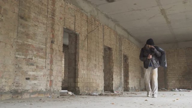 Sick vagabond walks with garbage bag in abandoned building