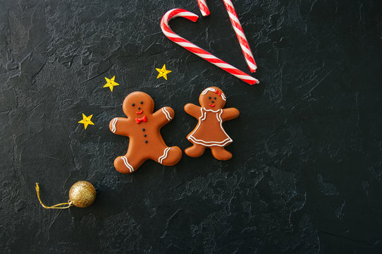 Festive Christmas background, Cookies with image of Gingerbread man and girl candy cane,  stars and ball on a black stone background. Top view with copy space.