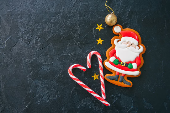 Festive Christmas background, Cookies with image of Santa, candy canes, stars and ball on a black stone background. Top view with copy space.