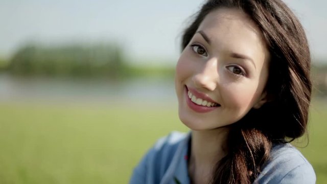Portrait of a beautiful girl long hair on the river bank. Woman stands on the shore and looking at camera.