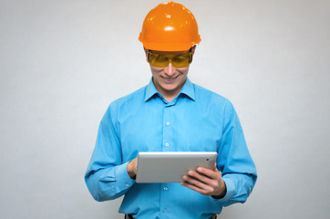 Happy builder worker in a hardhat using a tablet computer in his hands and smiling isolated. Engineer learning construction plans.