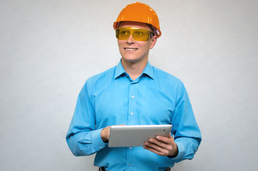 Happy builder worker in a hardhat using a tablet computer in his hands, smiles and looks up isolated. Engineer learning construction plans.