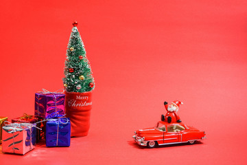 クリスマスに挨拶するミニチュア自動車に乗ったサンタクロース　赤背景