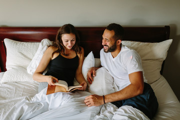Mixed race couple in bed laughing and reading a book