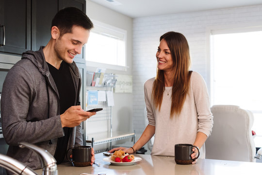 Happy Couple In Kitchen Talking And Checking Cell Phone