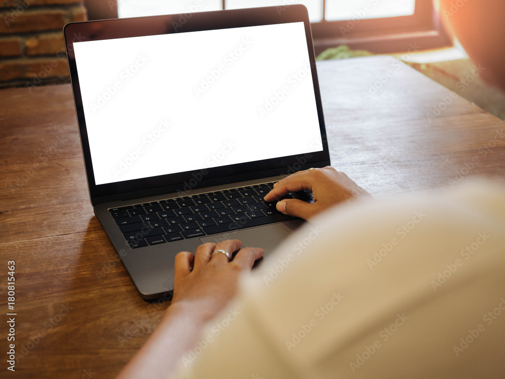 Poster closeup of the hands are using laptop keyboard with blank white screen on wood table at coffee cafe.