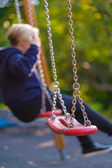 Modern equipped kids playground in sunny day. Child on chain swing
