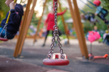 Modern equipped kids playground in sunny day. Kids and parents on chain swings