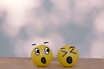 Two happy smiley yellow balls with surprise face on wooden table, bokeh wall background with copy space