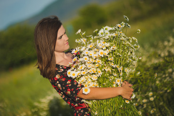 Charming adorable young lady woman dark brunette hairs and green eyes tender sexy posing with flowers wreath on head top and huge bouquet of wild daisy chamomile wearing stylish dress.