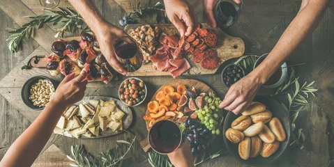 Zelfklevend Fotobehang Flat-lay of friends eating and drinking together. Top view of people having party, gathering, celebrating at wooden rustic table set with various wine snacks and fingerfoods. Hands holding glasses © sonyakamoz